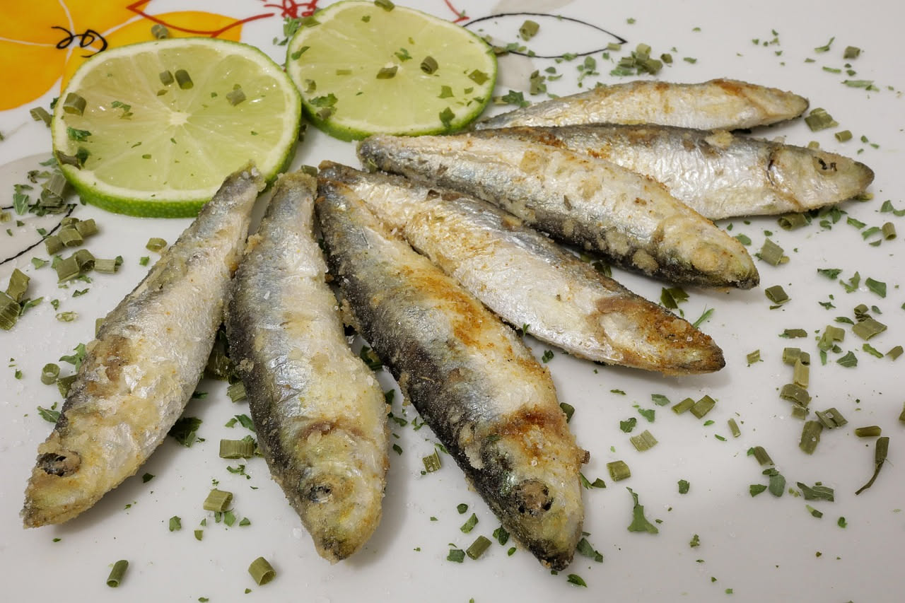 Acciughe in saòr su un piatto bianco con cipolla caramellata, pinoli e uvetta, condimento lucido di aceto balsamico.