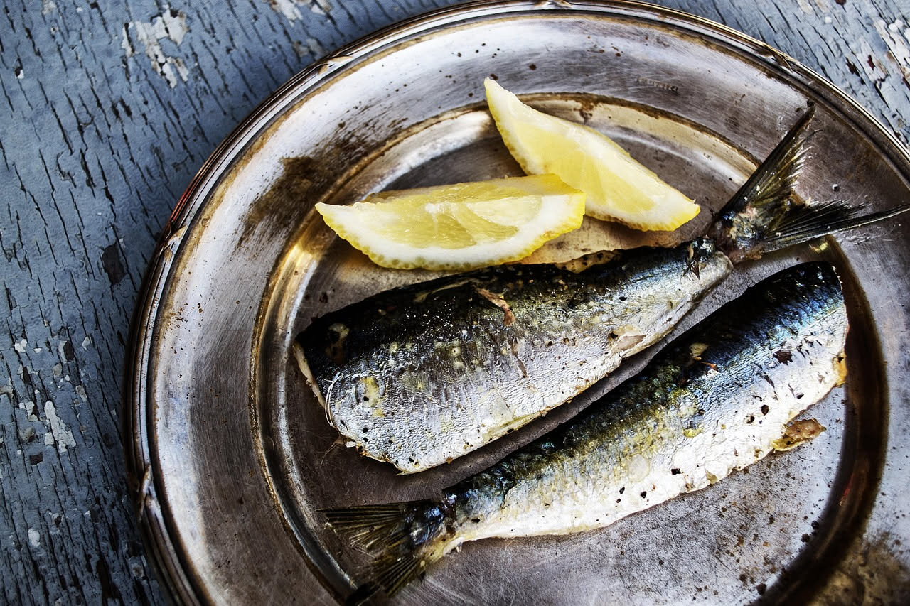 Alici bianche filettate su un piatto bianco con fettine di limone giallo, prezzemolo verde fresco e olio d'oliva che brilla