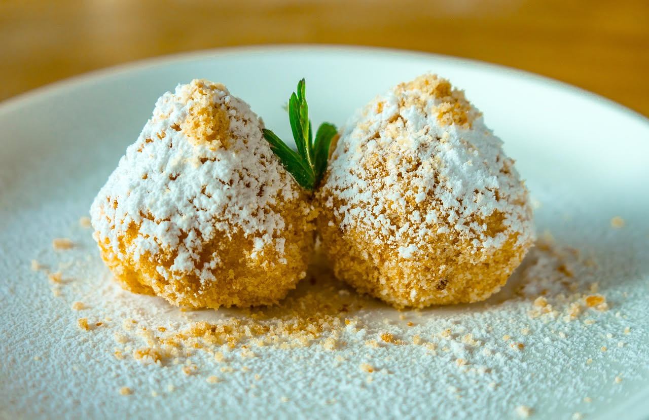 Tre arancini di Modica tondeggianti dorati in primo piano su un piatto bianco, con una fetta tagliata che mostra il ripieno di ragù e piselli gialli