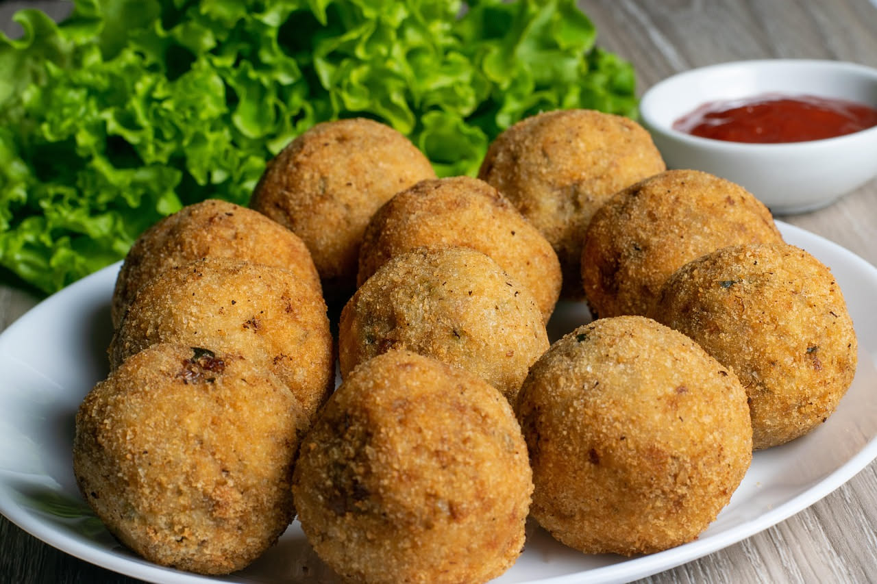 Tre arancini trapanesi tondi e dorati, appena fritti, con la panatura croccante e il ripieno di ragù visibile da una sezione tagliata in mezzo