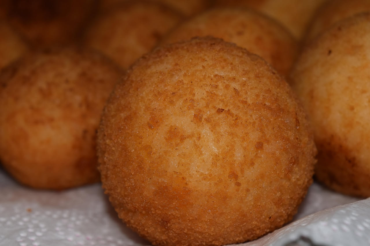 Arancino al burro dorato e croccante, tagliato a metà per mostrare il ripieno di ragù, piselli e mozzarella filante, su piatto bianco