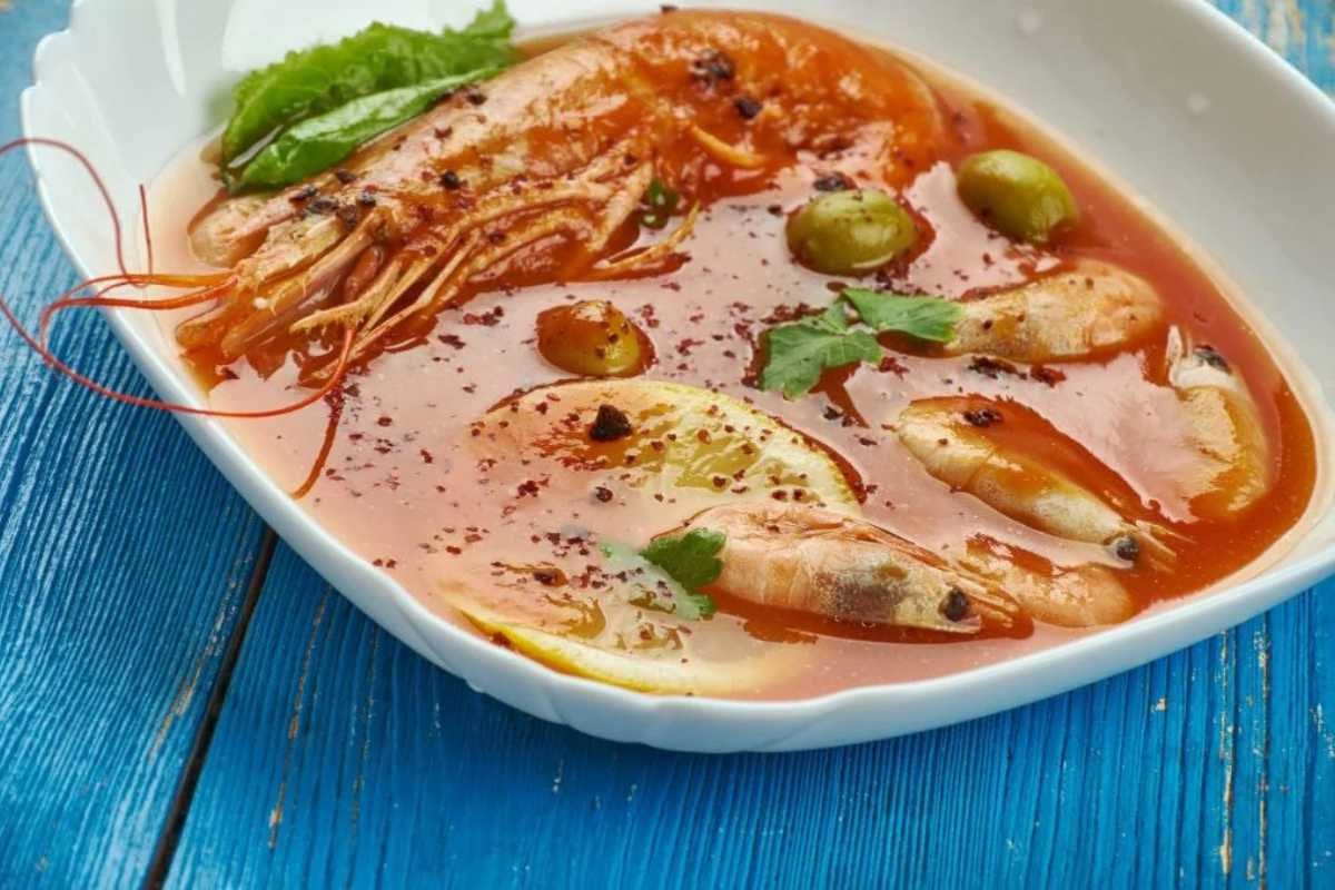 Zuppa di pesce brodetto salernitano in ciotola bianca con pezzi di pesce bianco, vongole e pomodoro, pane tostato a fianco, erba cipollina e olio d'oliva