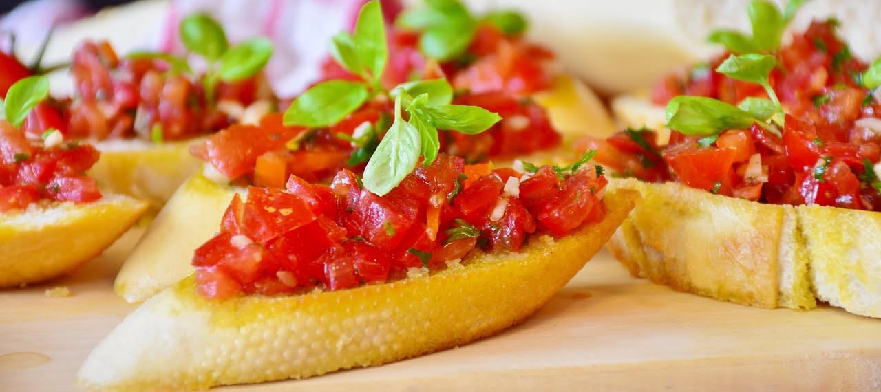 Bruschetta al pomodoro su un piatto bianco con pane tostato dorato, pomodori rossi brillanti, fettine di aglio e gocce di olio di oliva, con foglioline di basilico