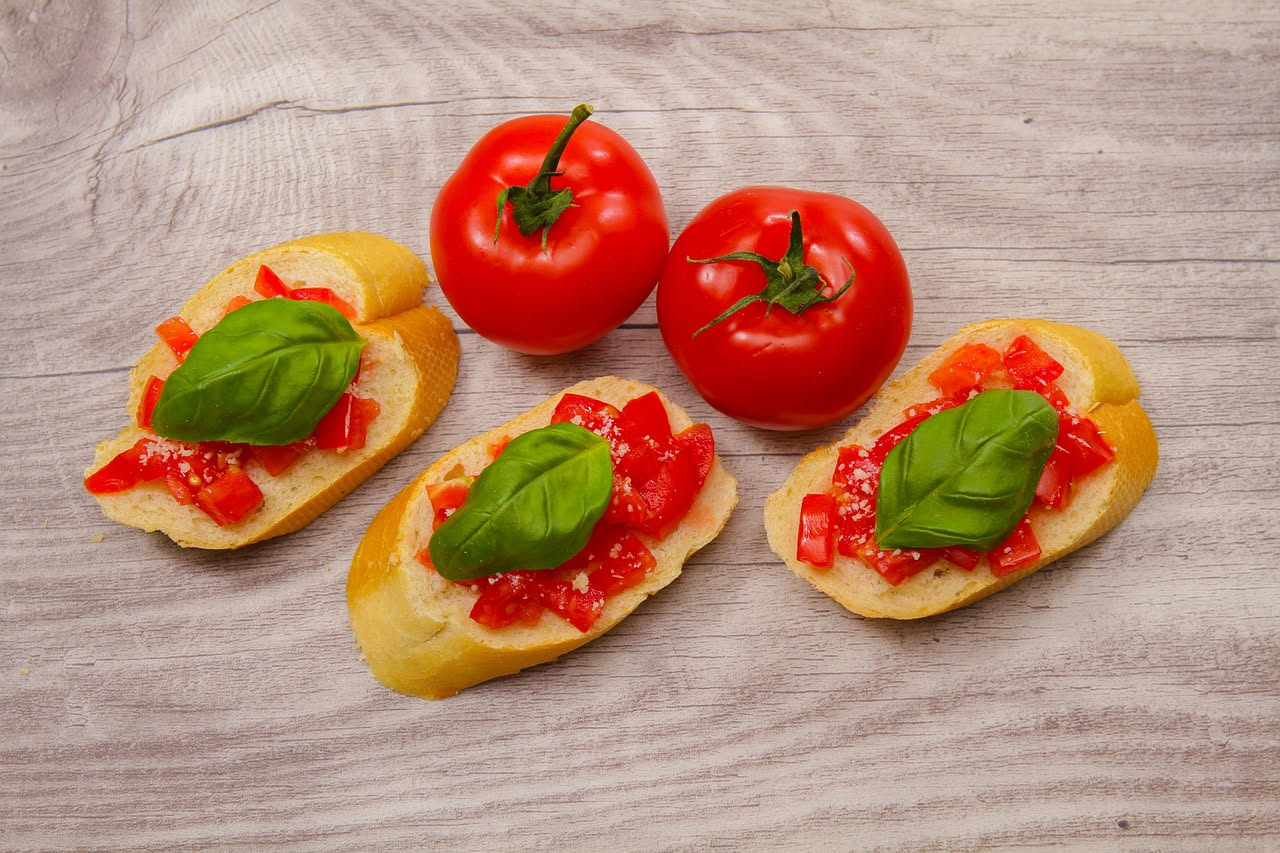 Fette di pane tostato con pomodori rossi tagliati, foglie di basilico verde e olio d'oliva su piatto bianco, vista dall'alto