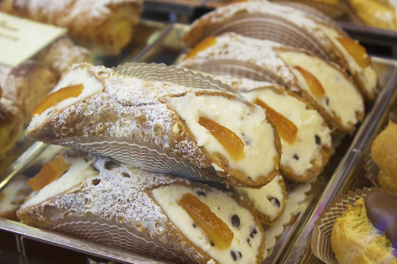 Buccellati di ricotta disposti su carta pergamena, dorati e glassati, con scorza d'arancia candita e mandorle intere visibili nel ripieno