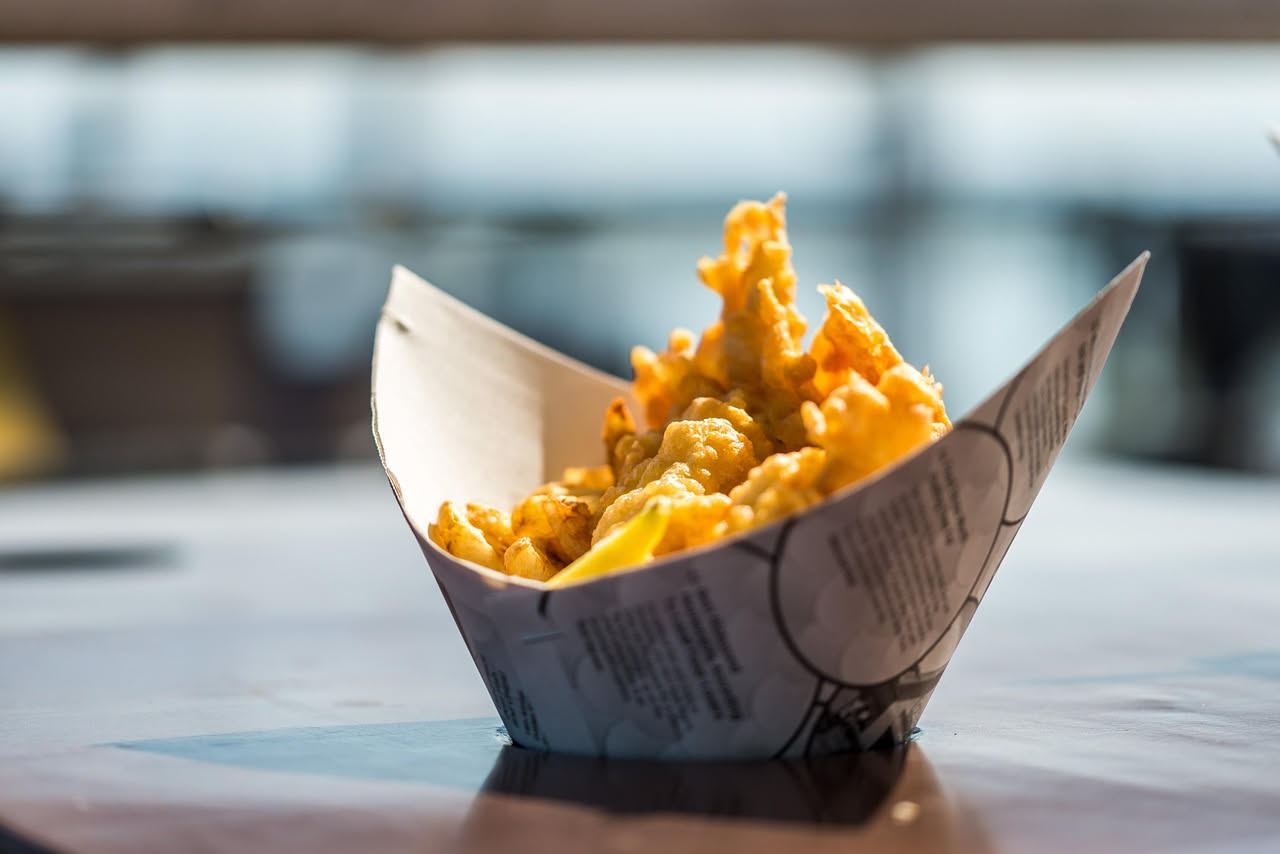 Cavolfiore dorato in pastella appena fritto su un piatto bianco, con interno bianco croccante visibile a una sezione, accompagnato da limone fresco