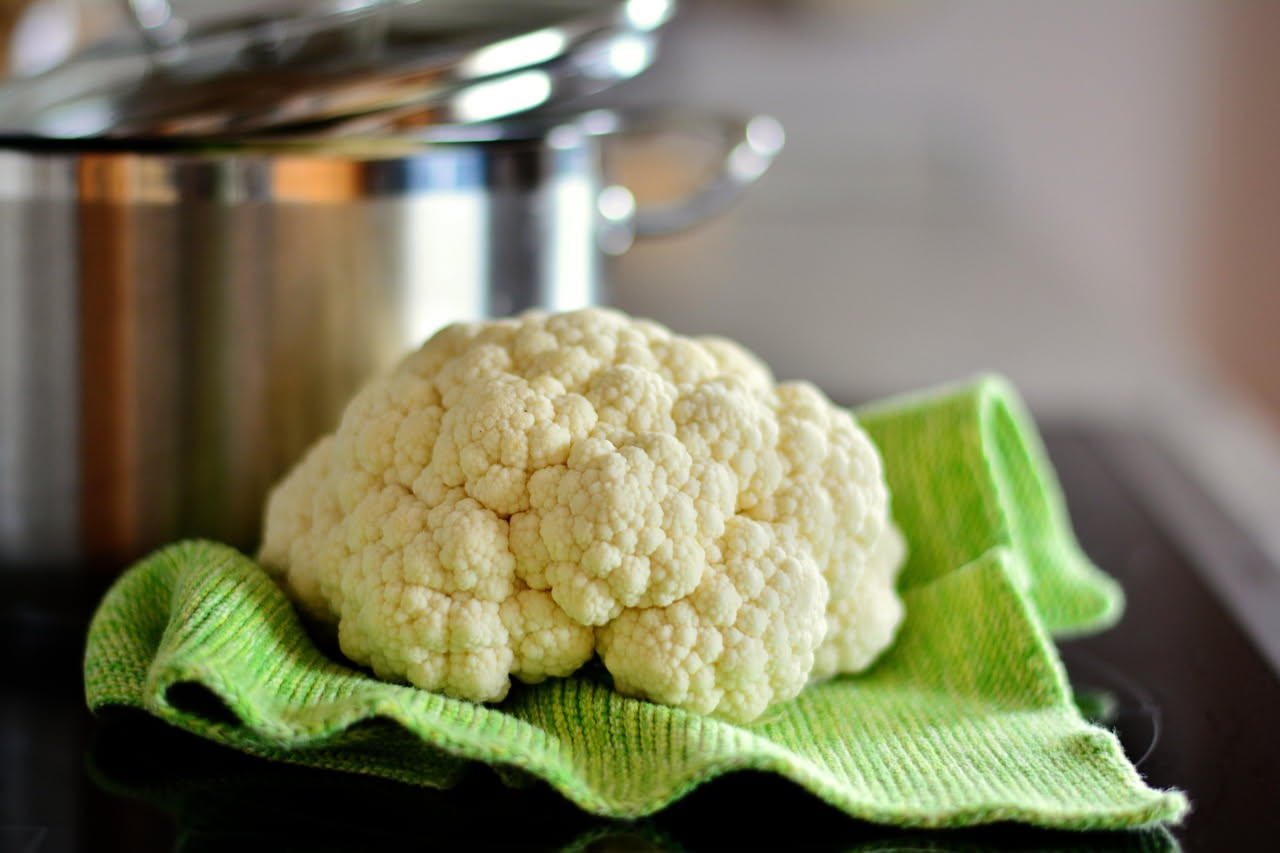 Cavolfiore in tempura dorato e croccante su carta assorbente bianca, con rosette color oro, accanto a una ciotola di salsa di soia