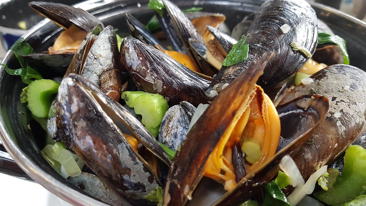 Cozze nere aperte ripiene di pangrattato dorato con prezzemolo verde su una teglia da forno bianca, ancora fumanti appena tolte dal calore