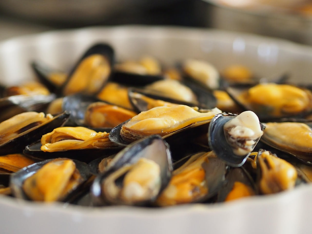 Cozze ripiene dorate in pirofila, ricoperte di pangrattato dorato, con gocce di olio d oliva e prezzemolo tritato fresco visibile in primo piano