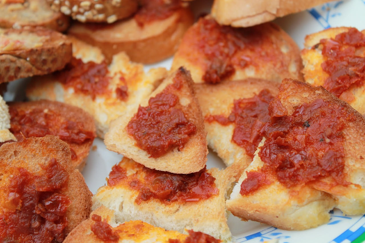Crostini dorati con ragù di carne macinata marrone scuro, grattugiata di parmigiano bianco e prezzemolo fresco verde, su piatto bianco