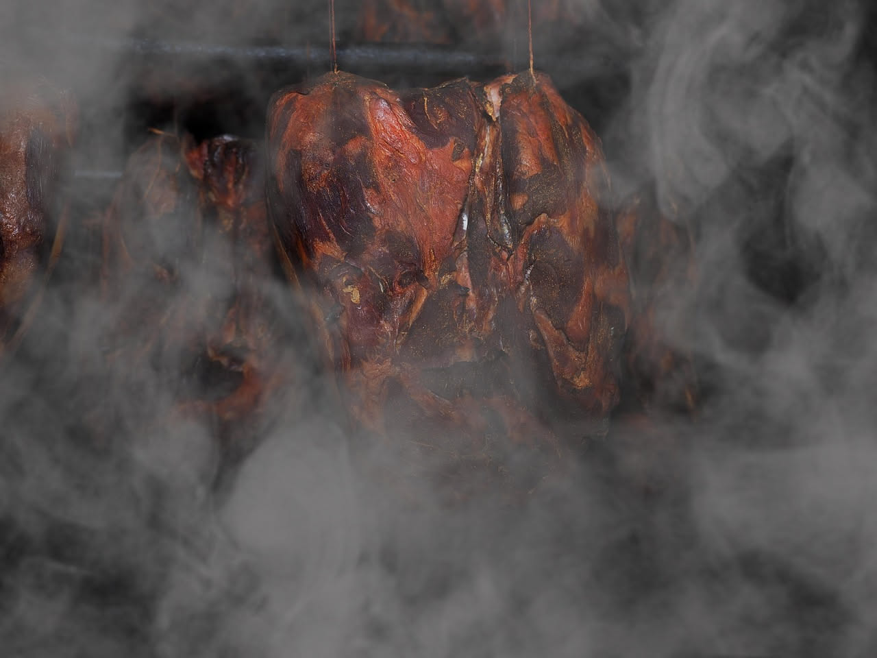 Fette di cuoppa affumicata su un tagliere di legno, carne rosso scuro con venature di grasso bianco e affumicatura in superficie