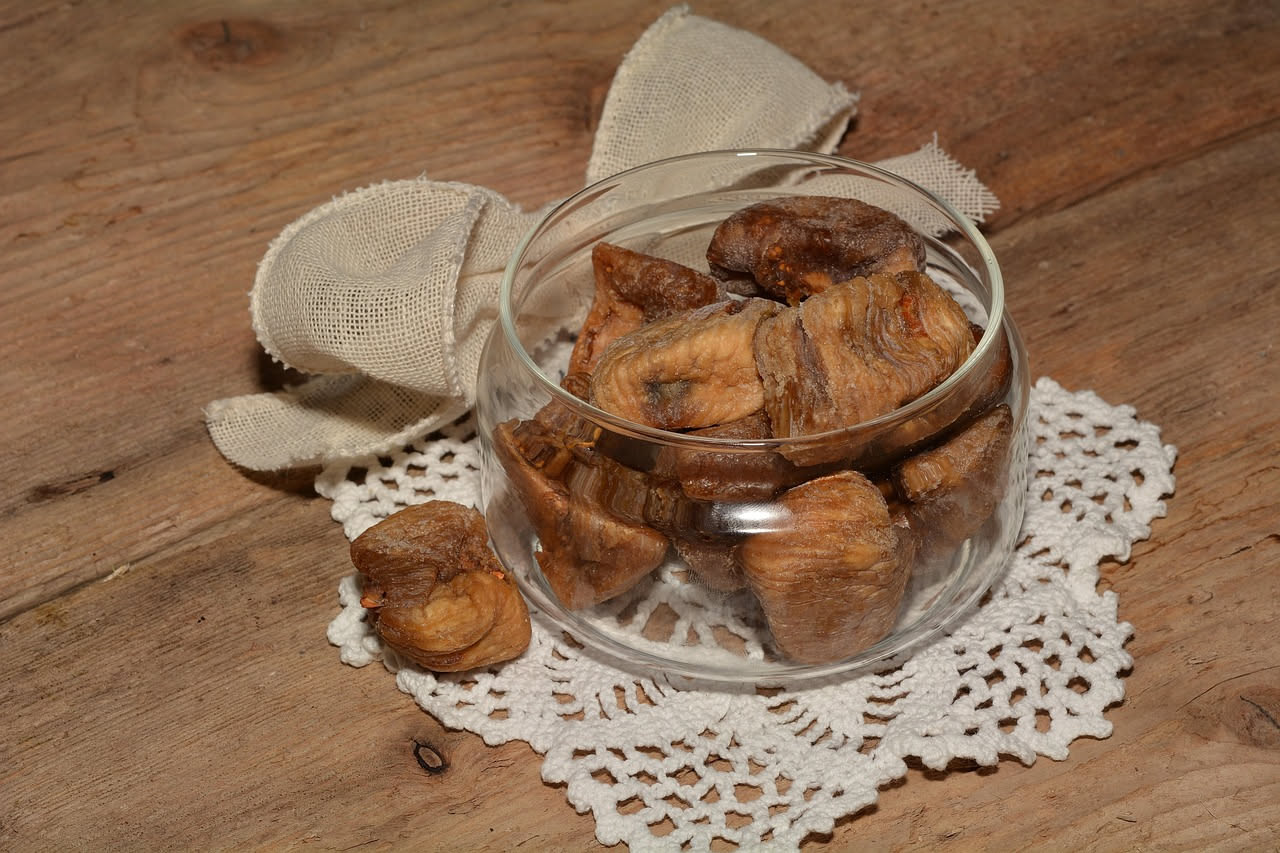 Quattro fichi secchi aperti a metà e ripieni di frutta secca tritata, disposti su un piatto di ceramica bianca con tovaglia di lino color nocciola