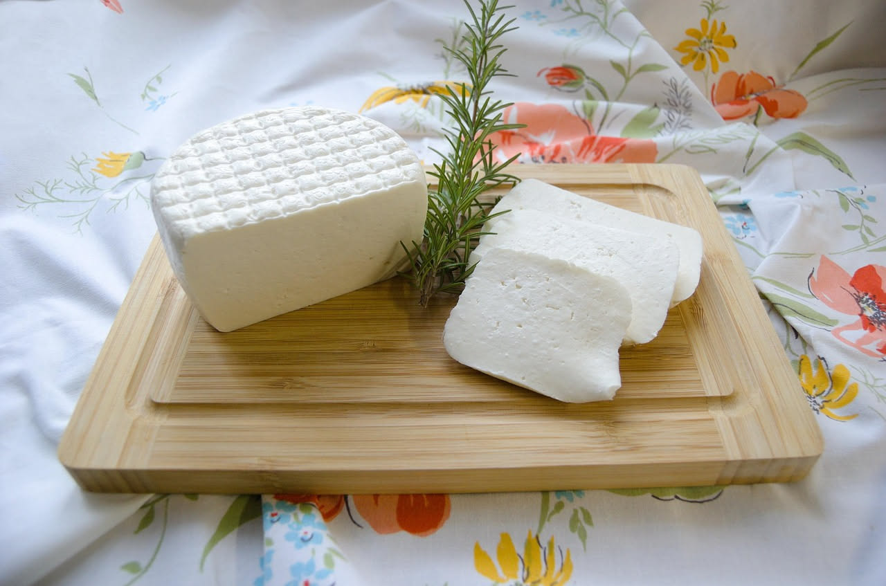 Formaggio di capra fresco bianco cremoso in una ciotola di vetro accanto a un bicchiere di latte di capra e una manciata di sale grosso
