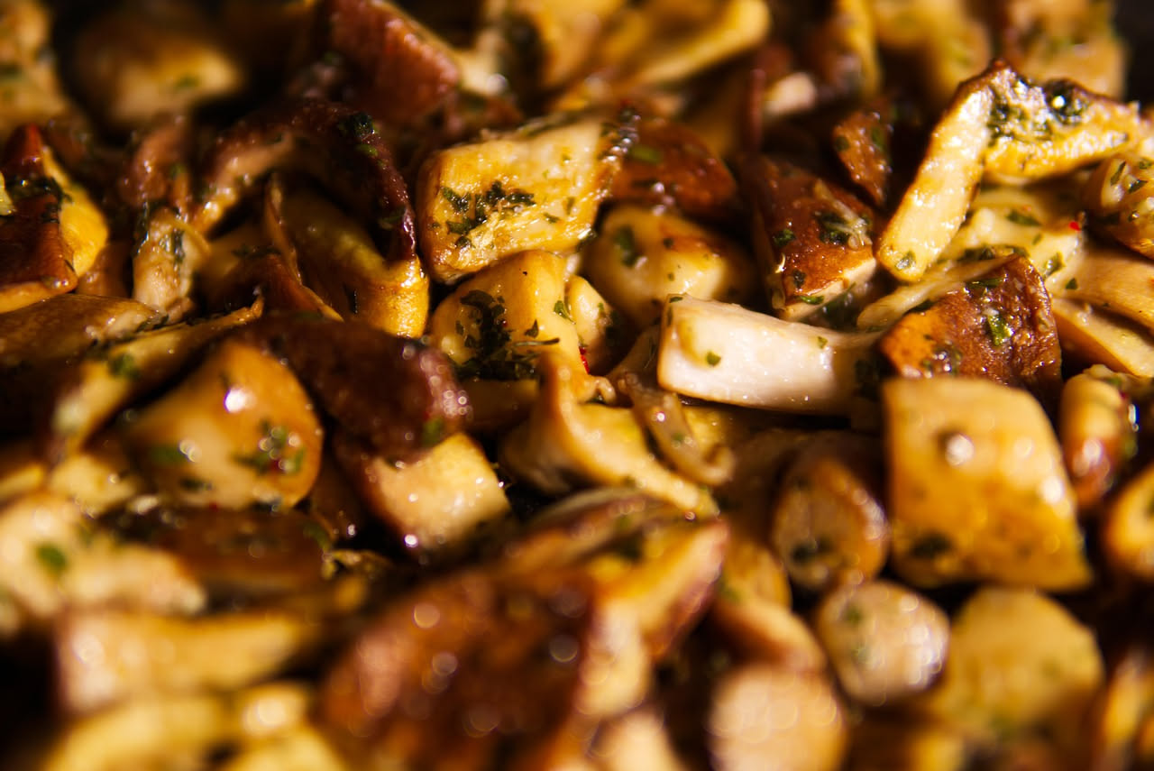 Funghi cardoncelli affettati e rosolati in padella con aglio e prezzemolo fresco, olio che luccica sui funghi dorati