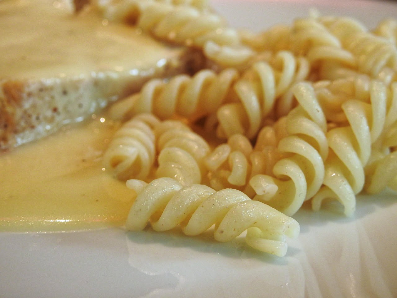 Piatto di fusilli ricoperti di salsa verde e rosso con pistacchio tritato, foglie di basilico fresco e gocce d'olio su fondo bianco