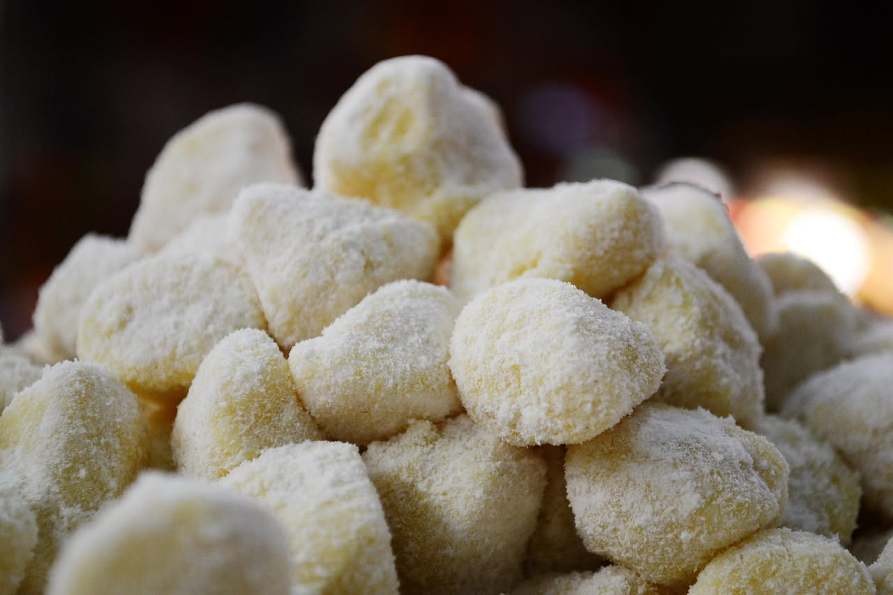 Gnocchi di ricotta fritti dorati e croccanti su un piatto bianco, ancora fumanti, serviti con un bicchiere di vino bianco