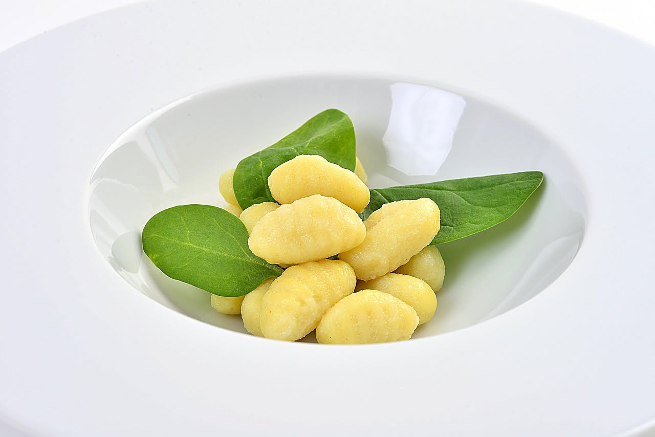 Gnocchi di ricotta e grano in un piatto bianco, conditi con burro fuso, parmigiano grattugiato e foglie di salvia fresca appena saltate