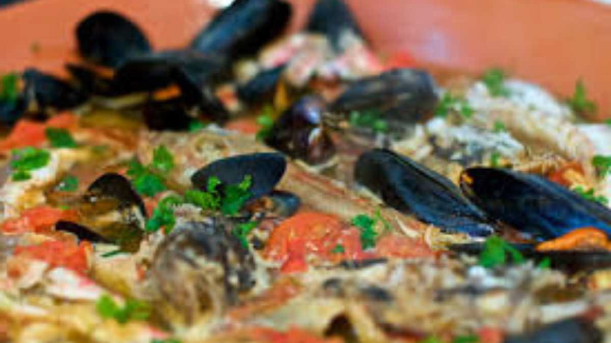 Brodetto di pesce in bianco piatto fondo con filetti di pesce bianco, vongole aperte, brodo fumante e prezzemolo verde fresco