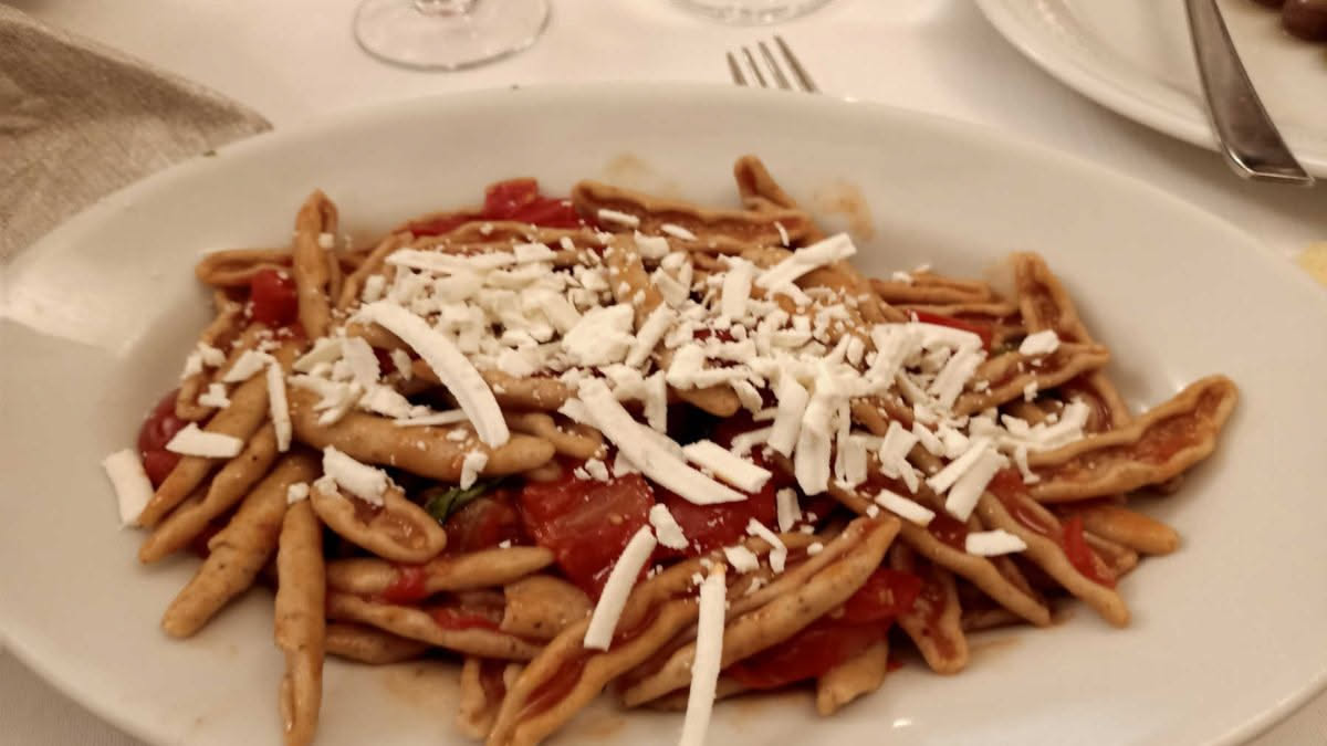 Peducci di pasta fresca, di colore giallo paglierino, irregolari e di varie lunghezze, disposti su un piatto bianco accanto a un cucchiaio di legno