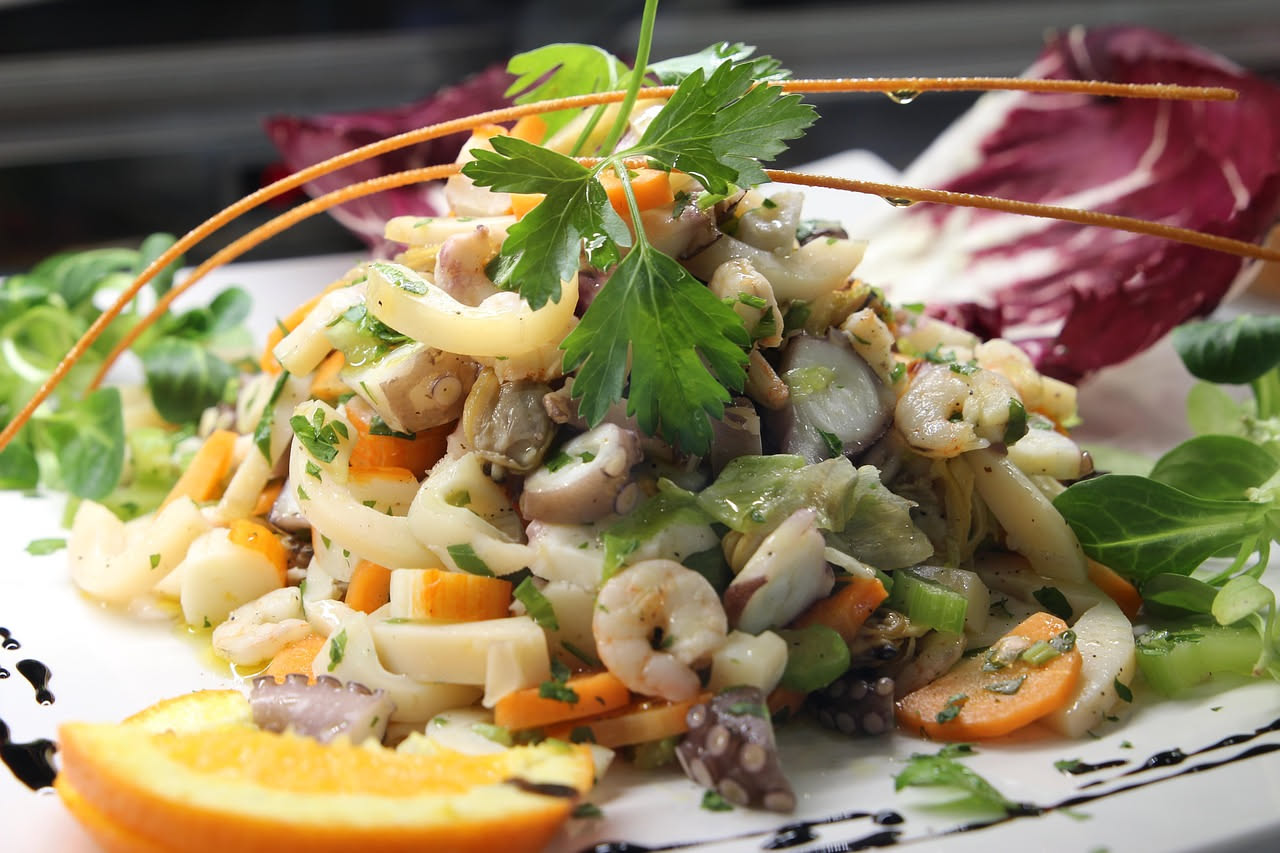 Insalata di frutti di mare in una ciotola bianca con gamberetti rosa, calamari bianchi, vongole e prezzemolo fresco su sfondo chiaro