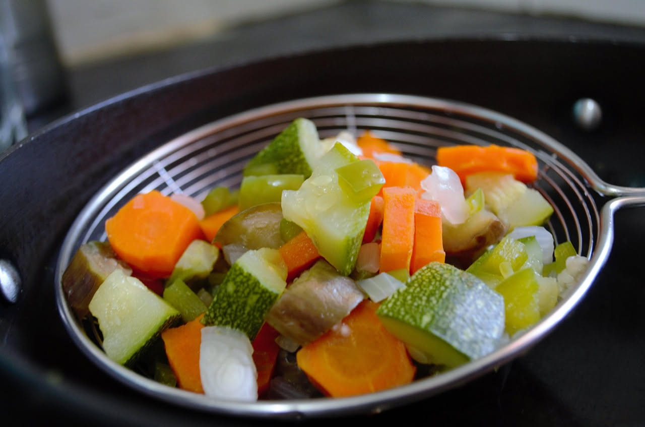 Insalata mista di verdure tagliate a pezzi uniformi in un contenitore di vetro con marinataincolor ambrato, carote, sedano, peperoni e cipolla visibili