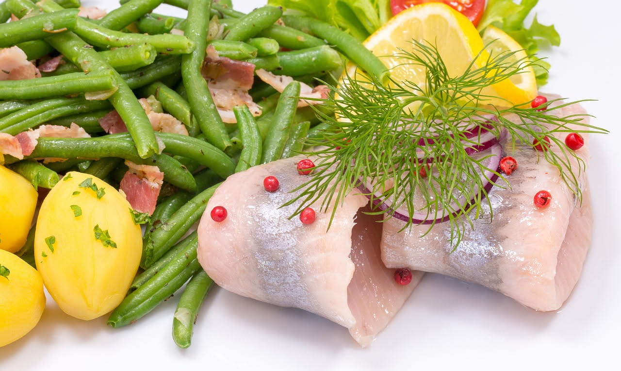 Involtini di alici disposti su un piatto bianco, arrotolati con ripieno di pangrattato e acciughe, conditi con olio e limone fresco