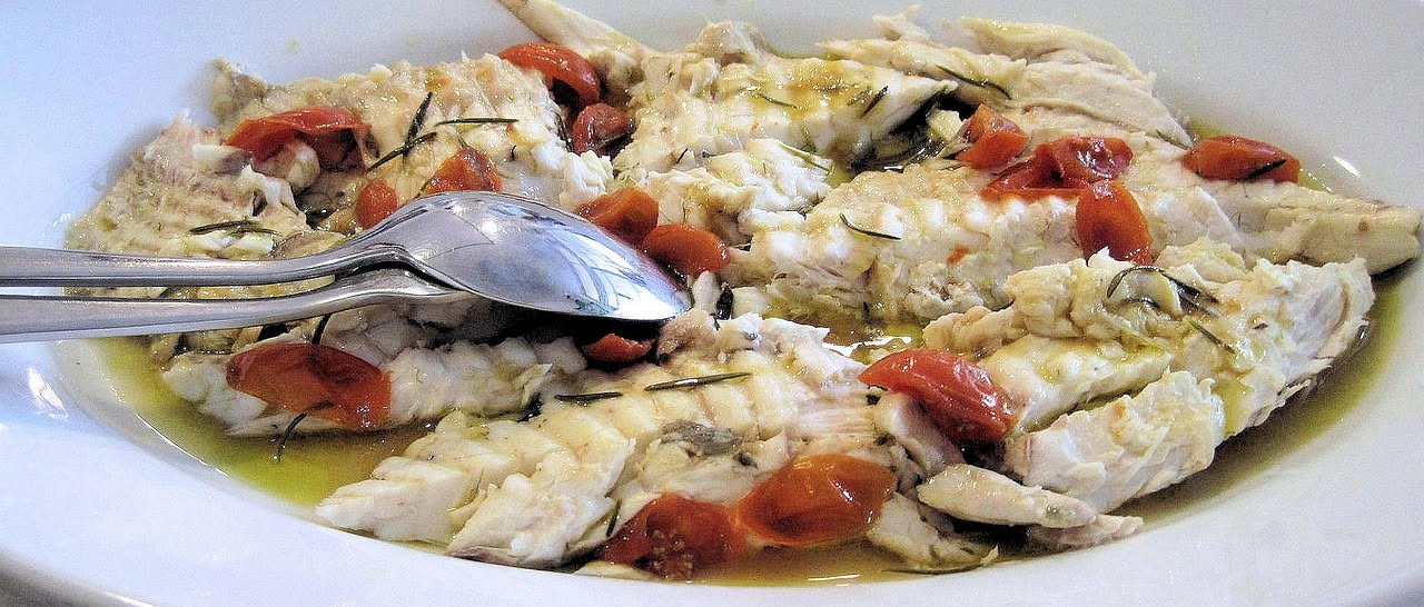 Filetti di pesce bianco marinati in un piatto bianco con fette di limone, olio d'oliva e sale grosso sparse in superficie