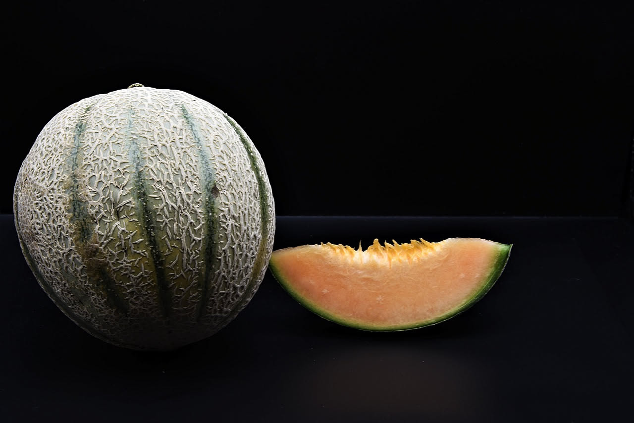 Fette di melone giallo disposto su un piatto bianco con granelli di sale grosso sparsi sulla polpa, sfondo sfocato di cucina luminosa