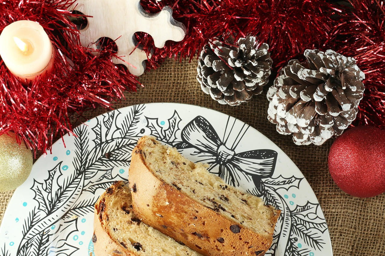 Musciamë affettato su un piatto di ceramica bianca, pane dolce color nocciola con pezzi visibili di uvetta e pinoli, sfondo in legno naturale