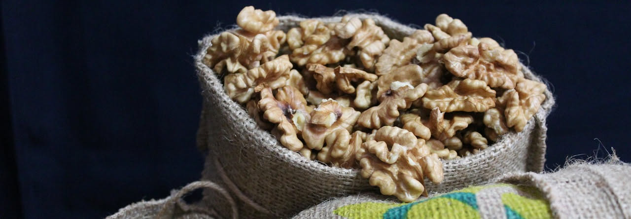 Noci tostate salate in un piattino bianco, con granuli di sale grosso visibili sulla superficie, sfondo di legno naturale