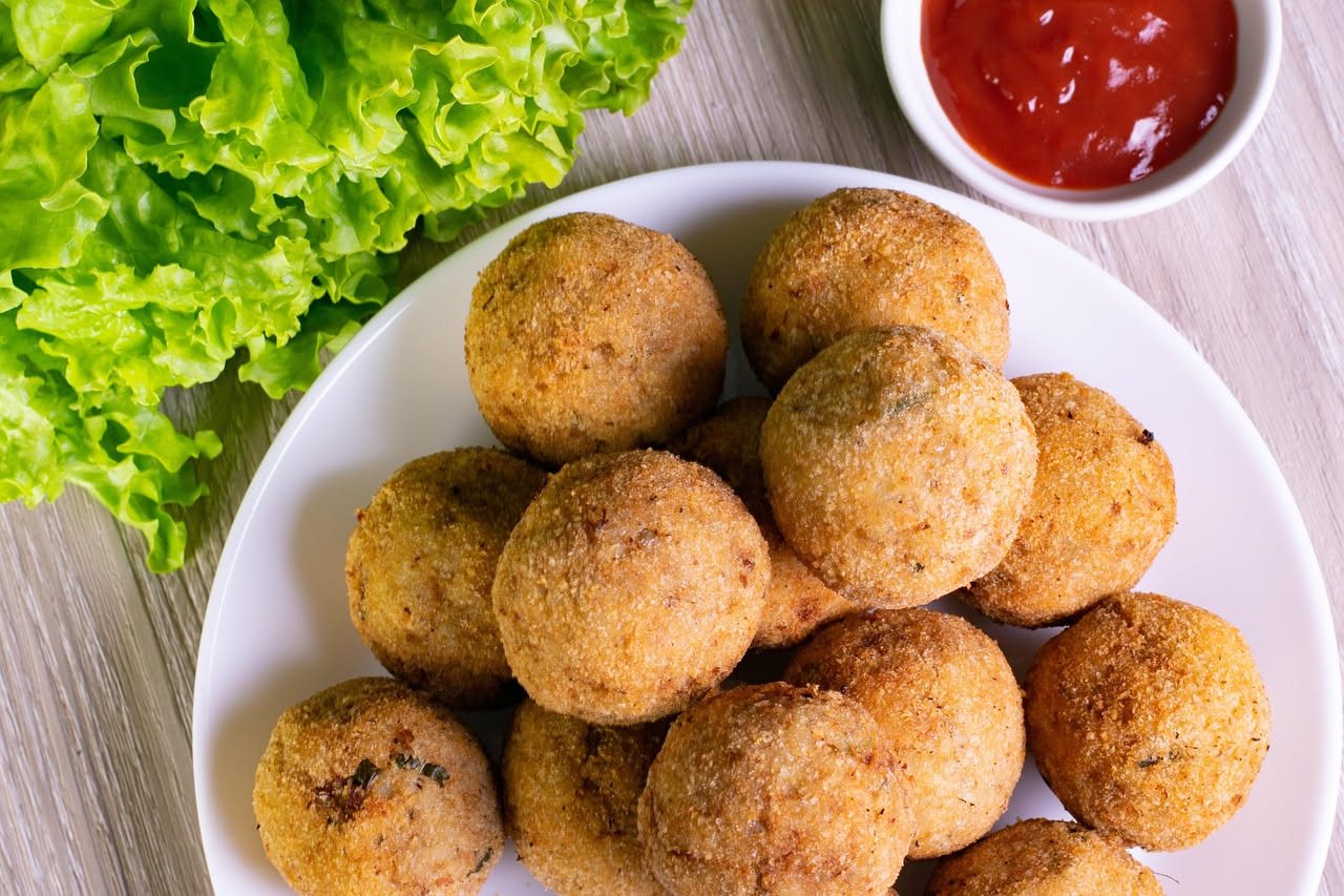 Olive grandi e tonde, dorate e croccanti, tagliate a meta per mostrare il ripieno di carne macinata rosa e pane. Su un piatto bianco con limone fresco accanto
