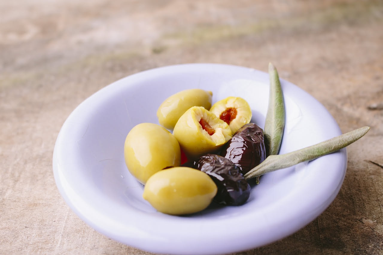 Ciotola bianca con olive taggiasche verdi cotte, condite con olio e prezzemolo fresco, su sfondo di legno naturale