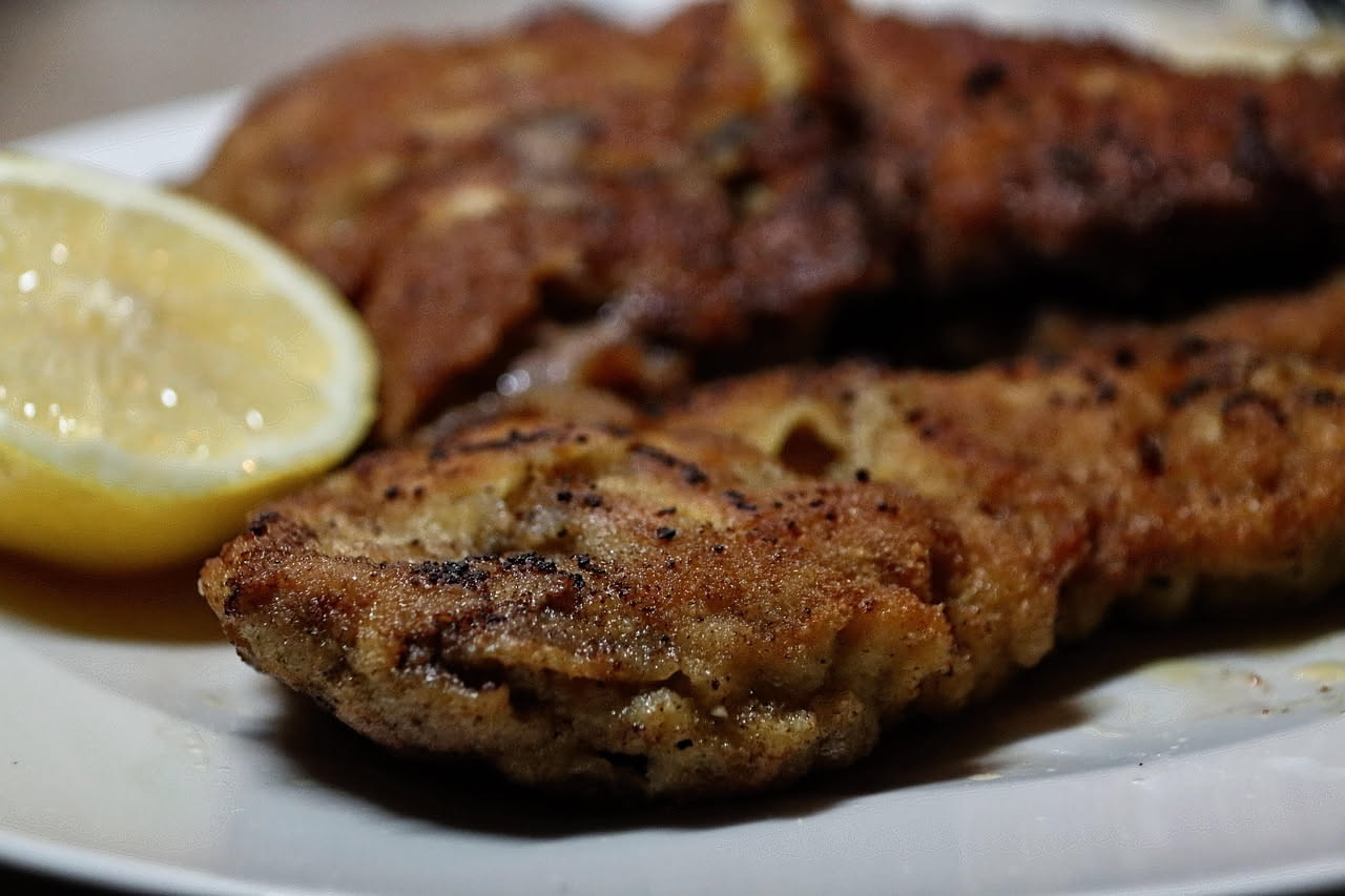 Organi di vitello fritti dorati e croccanti su un piatto bianco, con una fetta di limone e prezzemolo fresco