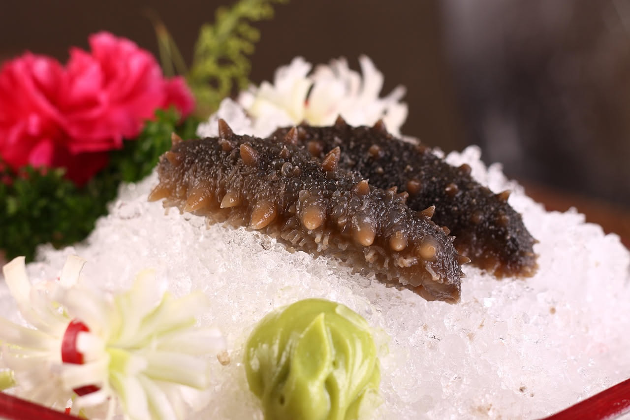 Ova di riccio di mare di colore arancione brillante in una ciotola bianca con due ricci di mare aperti e un cucchiaio d'acciaio su fondo grigio