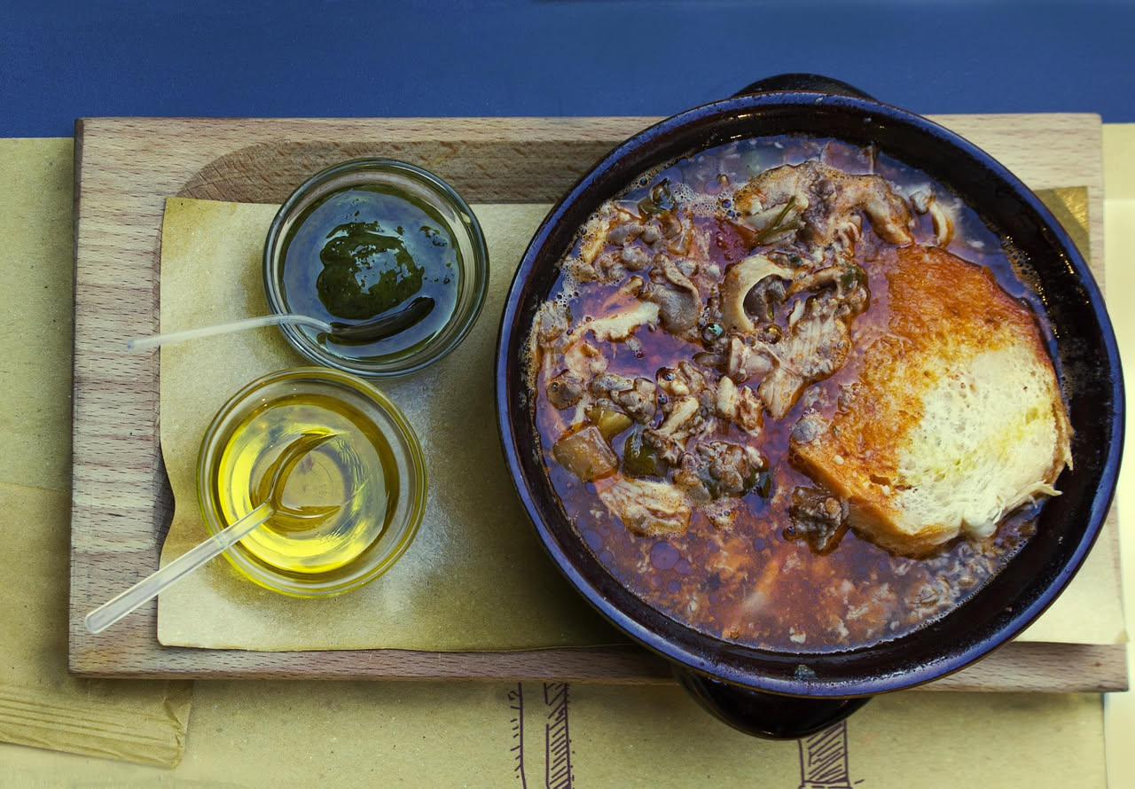 Ciotola di ceramica bianca con zuppa trasparente, uova filate gialle, fette di pane tostato galleggianti, vapore leggero, cucchiaio di legno