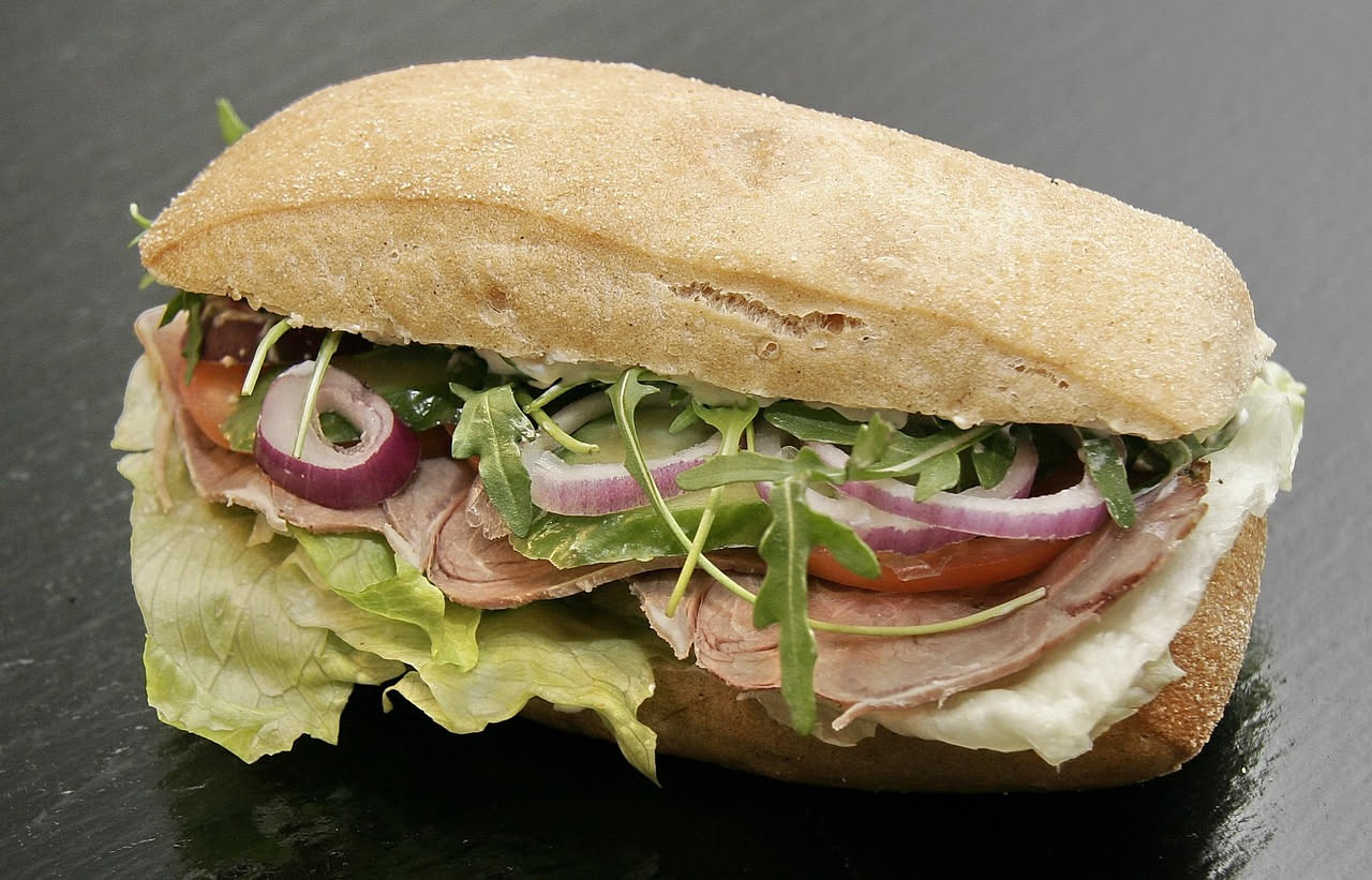 Panino con la milza affettata e dorata, dentro un pane morbido tondo, con una fetta di limone al fianco, su sfondo chiaro