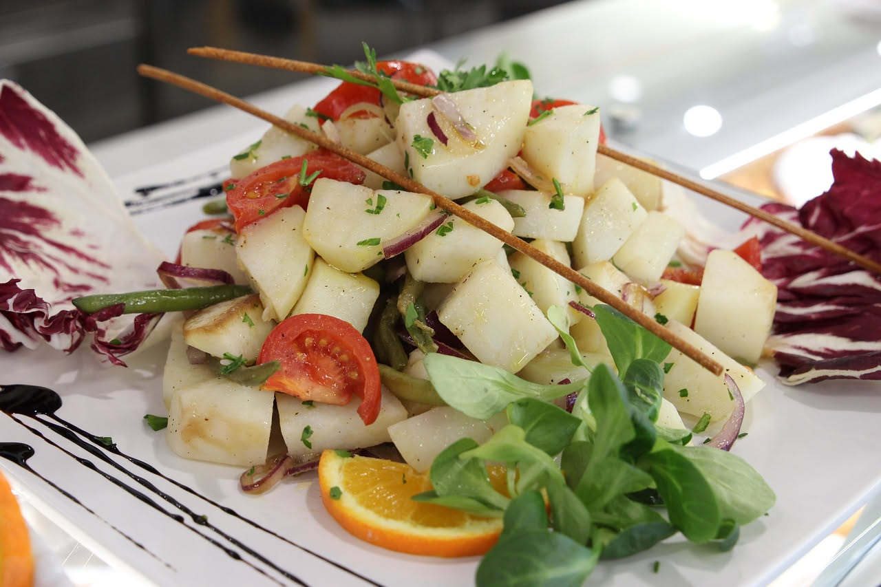 Insalata di pane panzanella con cubetti di pane tostato, pomodori rossi freschi, cipolle bianche, cetriolo affettato e foglie di basilico verde in una ciotola bianca, condita di olio