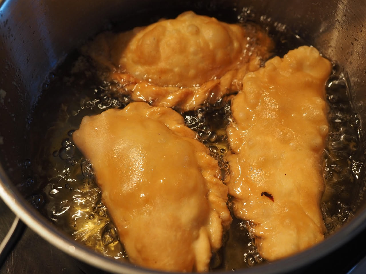 Panzerotti napoletani appena fritti, dorati e croccanti, infilzati su carta assorbente con ragù rosso e mozzarella filante visibili all'interno