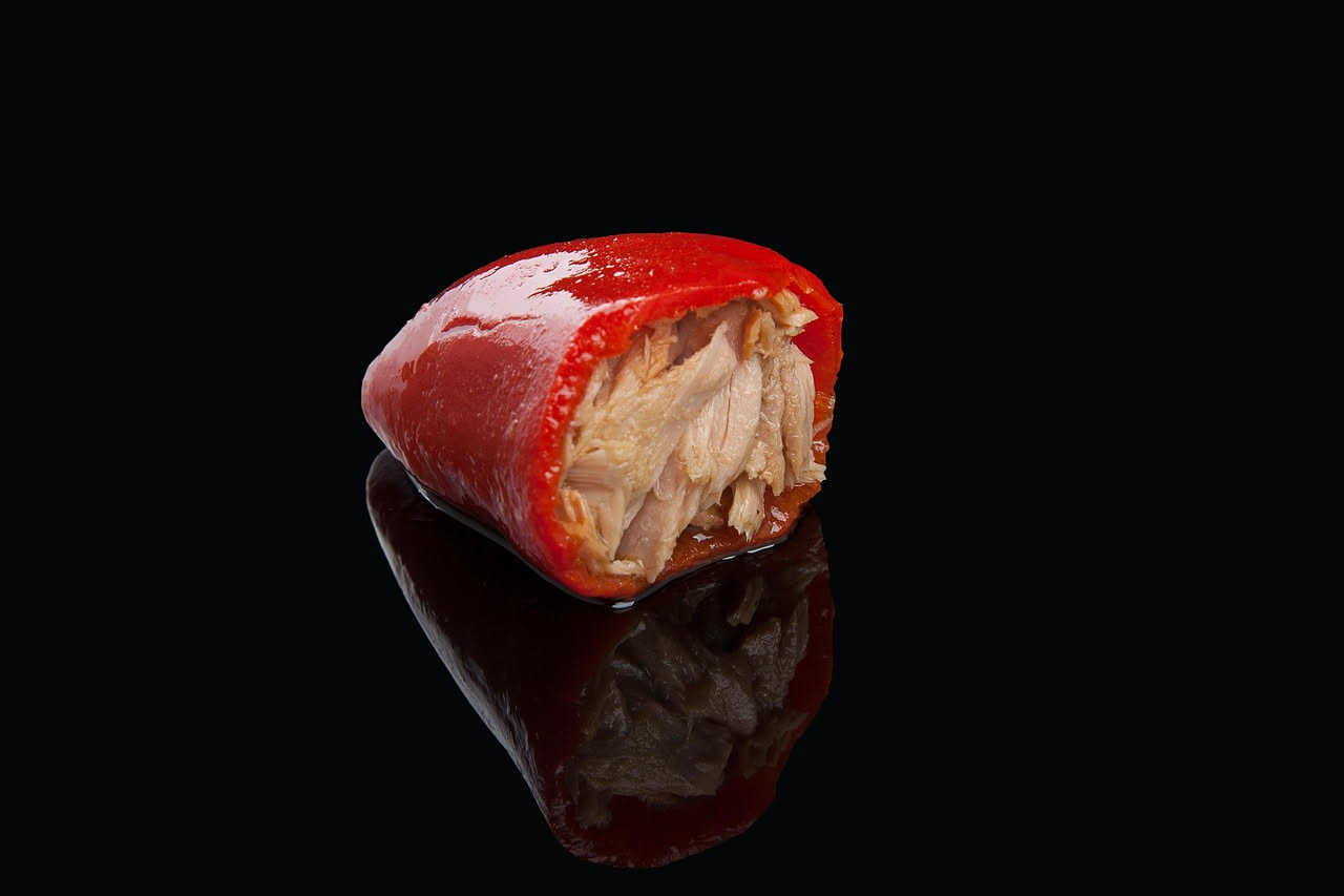 Tre peperoni rossi ripieni di carne macinata e riso, cotti in umido in una pentola di terracotta con sugo di pomodoro, visti da vicino