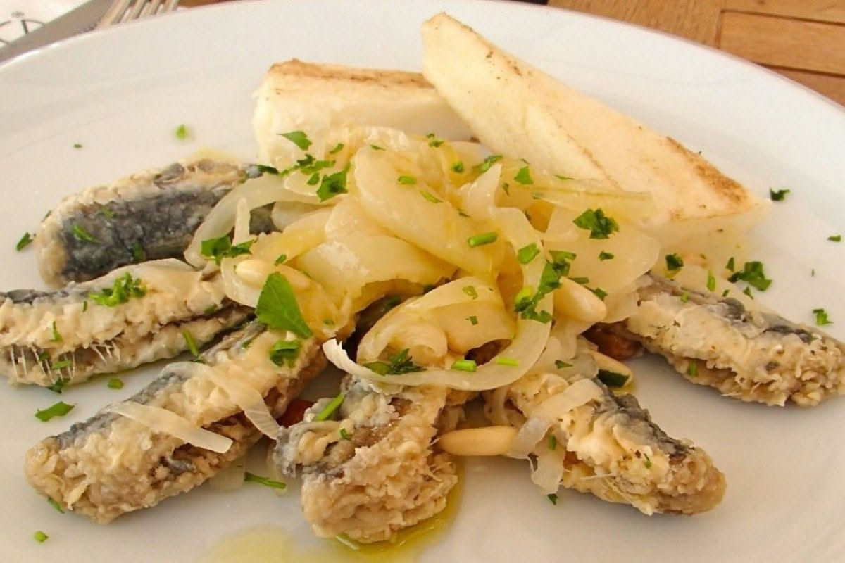 Piatto di pasta con sarde fritte intere, pomodoro rosso, finocchio selvatico e peperoncino, su tavolo in legno
