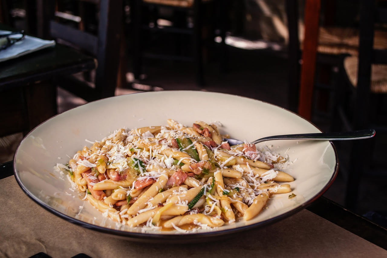 Piatto di pasta chi sardi con pasta gialla per lo zafferano, guarnita di formaggio grattugiato bianco, su un fondo di legno scuro con un cucchiaio di legno a lato
