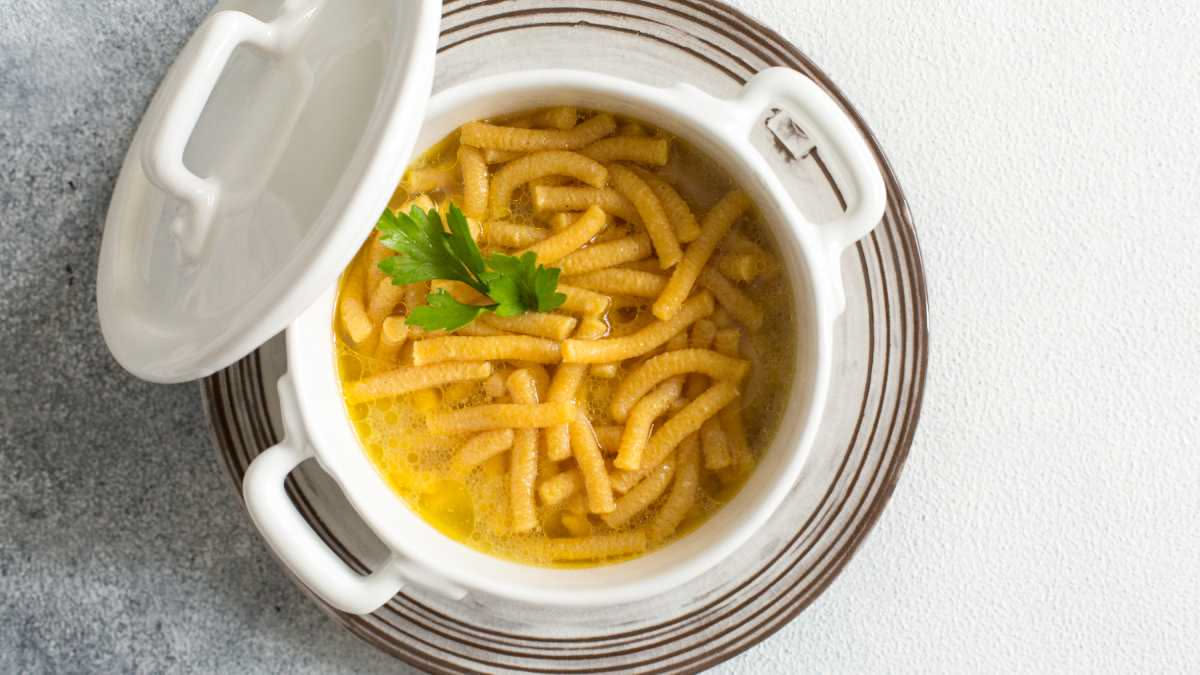 Ciotola di pasta e fagioli fumante con olio d'oliva versato sopra, fagioli borlotti e tubetti, servita in piatto bianco su tavolo di legno