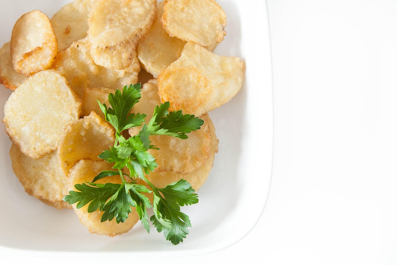 Patate fritte dorate e croccanti in un contenitore di carta bianca, vapore ancora visibile, sale grosso sparso sulla superficie