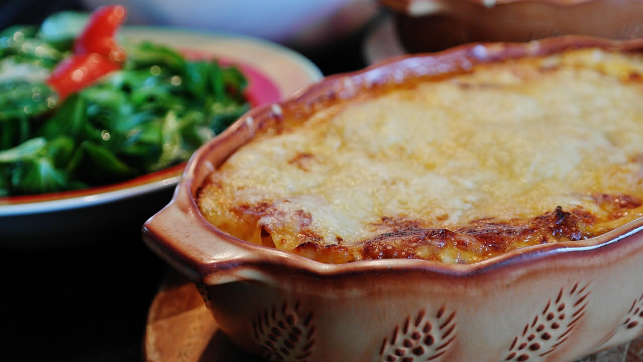 Piatto di patate gratinate con formaggio dorato in superficie, ancora fumante, con salsa cremosa visibile tra gli strati di patate tagliate sottili