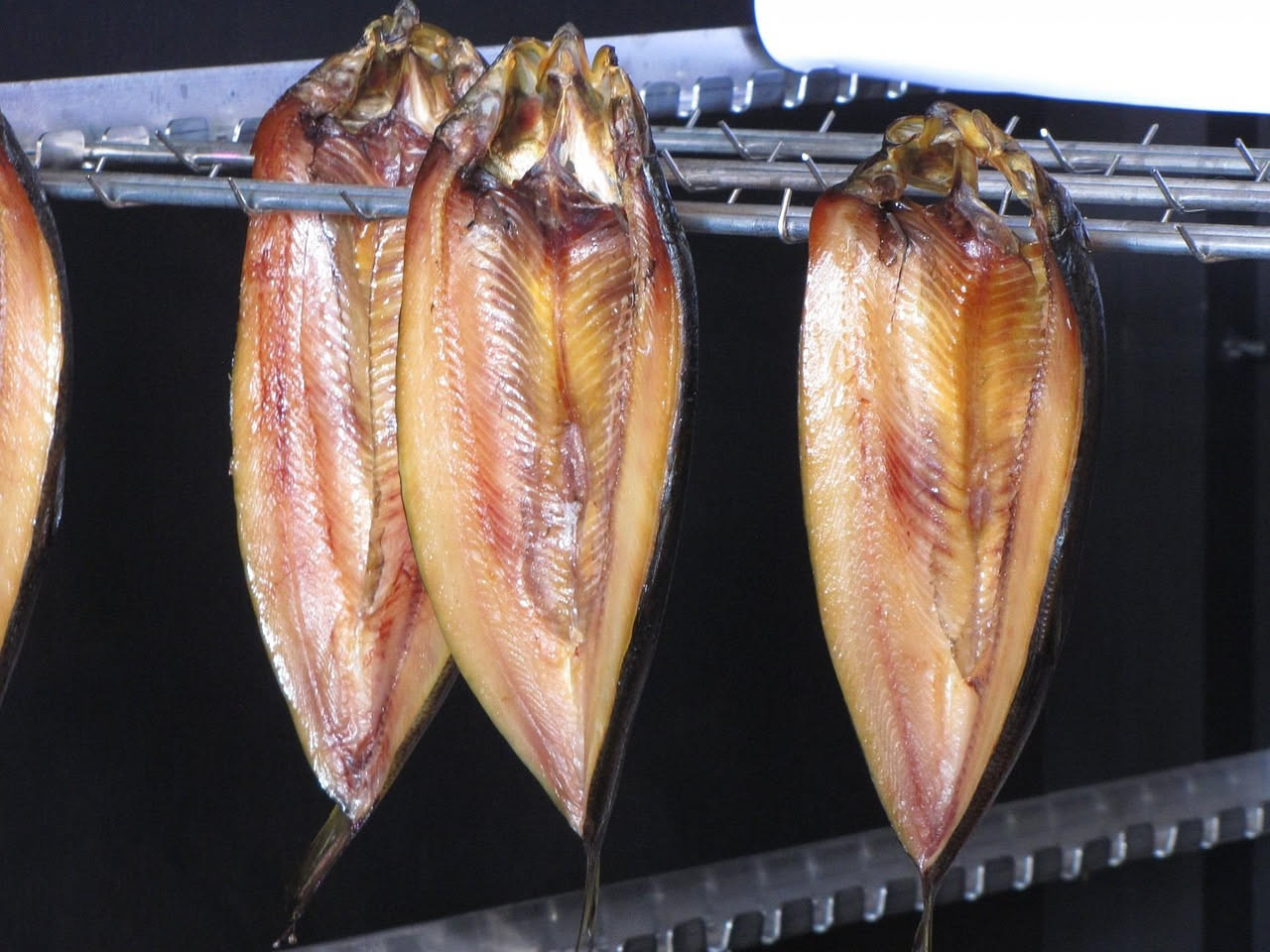 Filetto di pesce affumicato dorato su carta da forno, con legno di faggio fumante sullo sfondo e un termometro da cucina