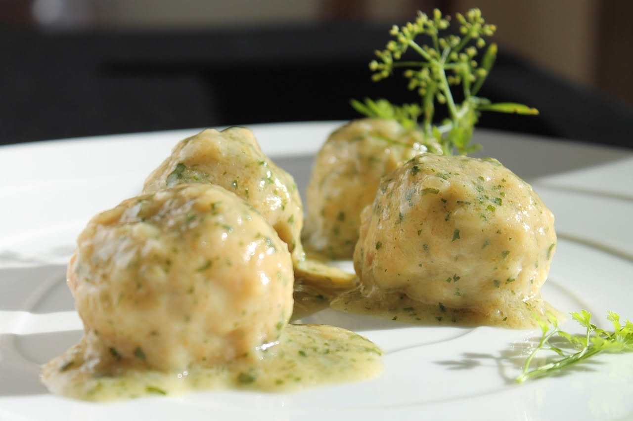 Polpettine di pesce dorate in un piatto bianco con limone fresco e prezzemolo, su sfondo di tavolo di legno chiaro
