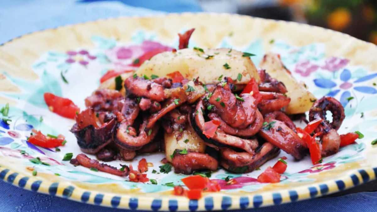 Polpo cotto in umido con pomodori rossi, olive nere e prezzemolo fresco in un piatto bianco, con tentacoli morbidi e rosati
