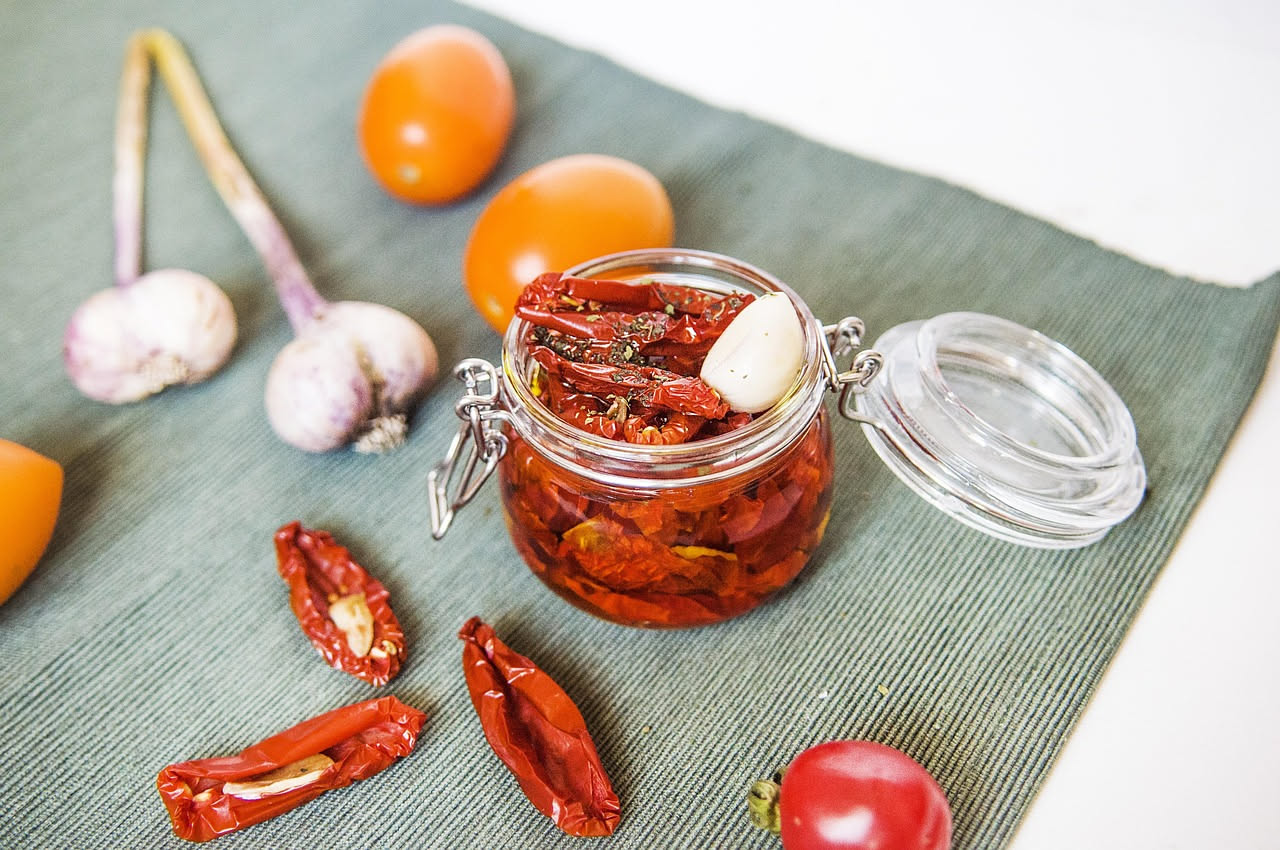 Pomodori rossi secchi tagliati a metà, disposti su un vassoio di carta da forno, alcuni ancora freschi accanto, in una cucina luminosa