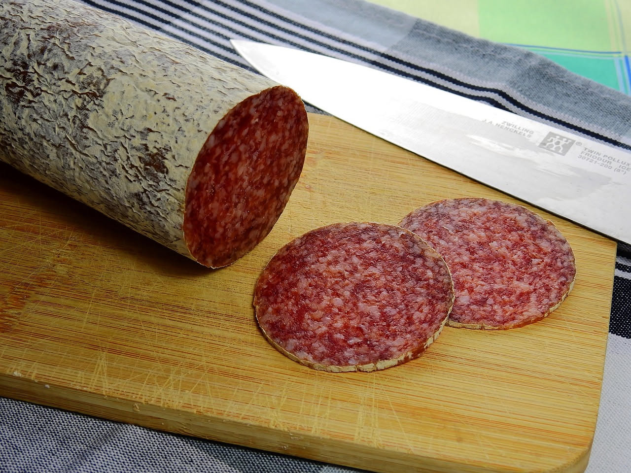 Fette di salame di Caserta tagliate finemente, di colore rosso scuro con grasso bianco, disposte su un piatto bianco con accanto un coltello da cucina