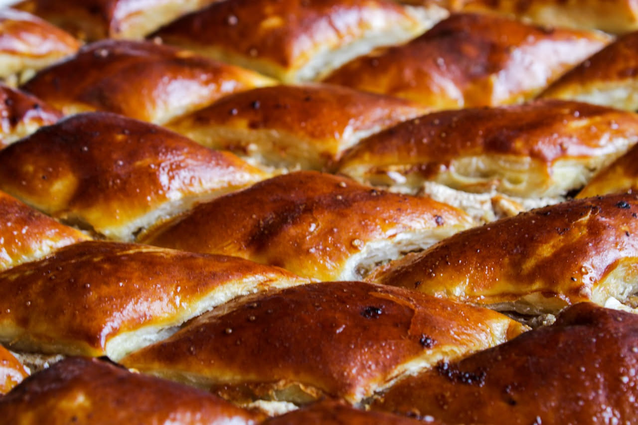 Scaccia trapanese dorata e croccante tagliata a fette quadrate su un tavolo di legno, con ripieno di cipolla caramellata, acciughe e olive verdi visibili in sezione
